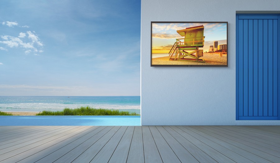 A SunBrite wall-mounted TV installed on a deck overlooking the ocean.  